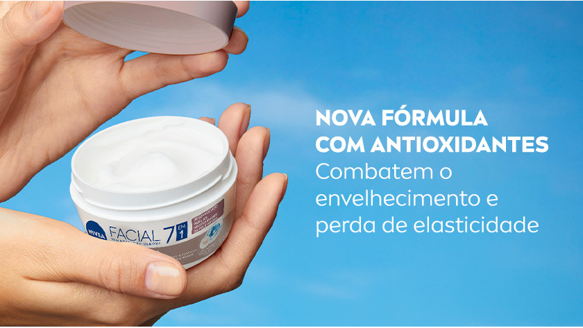 Fundo azul com nuvens. Mãos seguram pote aberto do creme NIVEA Facial 7 em 1 com rótulo branco e cinza, destacando a textura do creme. À direita, texto em branco destaca nova fórmula com antioxidantes que combatem o envelhecimento.