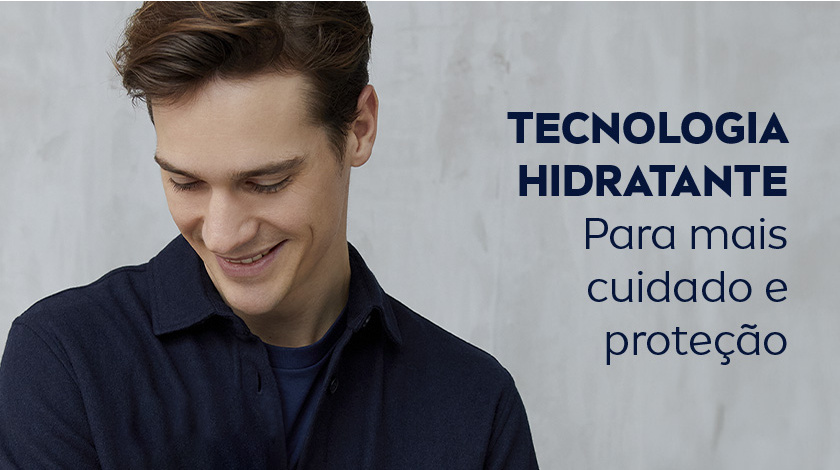 Homem jovem sorrindo e olhando para baixo, vestido com camisa azul.