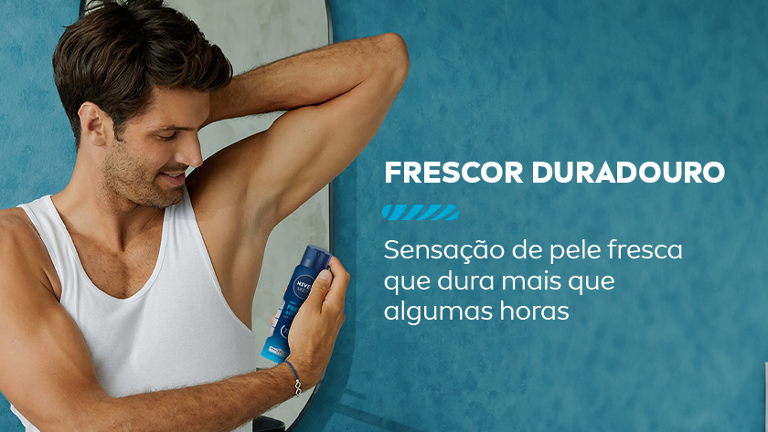 Frescor duradouro Sensação de pele fresca que dura mais que algumas horas. Um homem sorri, enquanto aplica o desodorante na axila, ele usa uma regata branca. Ao fundo, um espelho com bordas redondas e um fundo azul.