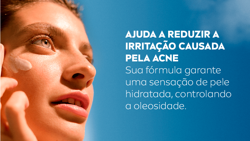 Close de uma mulher com pele iluminada aplicando creme no rosto com o dedo indicador. O fundo é um céu azul claro.