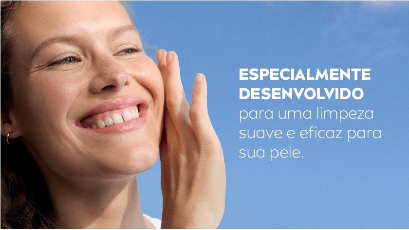 Mulher sorrindo, enquanto coloca a mão no rosto. O fundo é um céu azul.