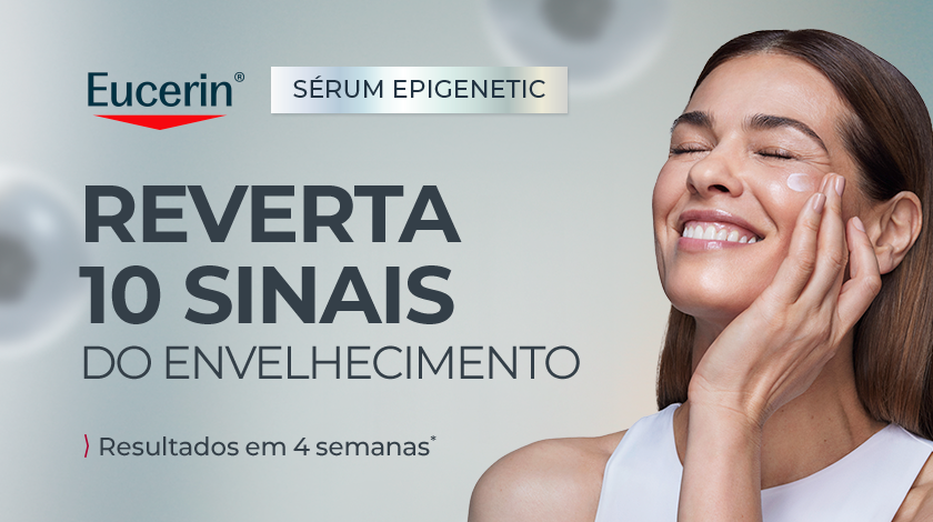 Mulher sorrindo suavemente aplica o produto no rosto. O fundo da imagem é prateado.