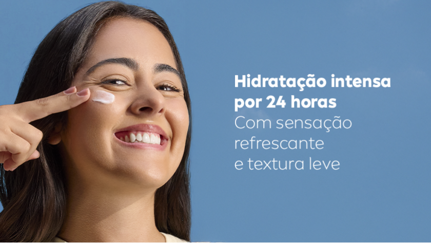 Fundo azul claro. Mulher sorridente aplica creme no rosto com o dedo indicador.