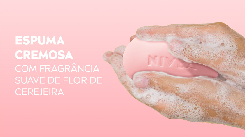 Mão segurando sabonete NIVEA rosa ensaboado, produzindo espuma cremosa sobre fundo rosa claro.