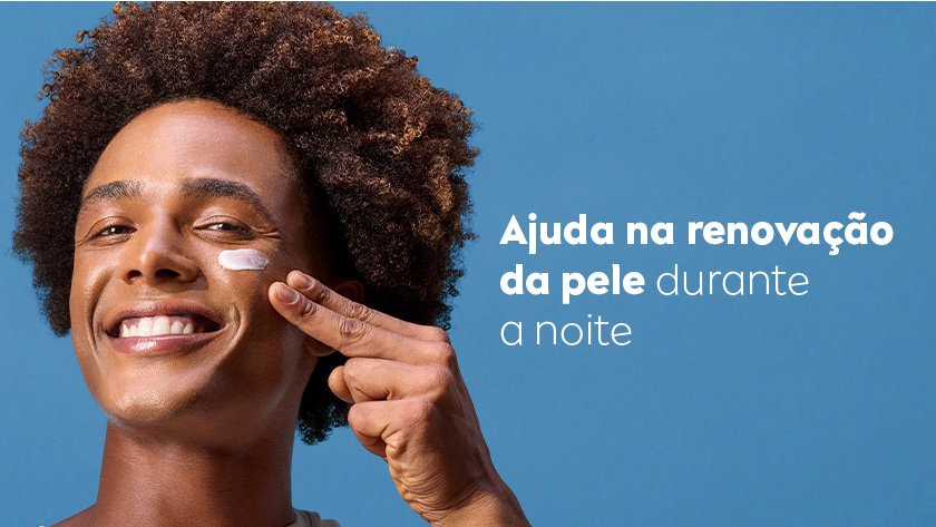 Fundo azul claro. Homem sorridente aplica creme no rosto com dois dedos. À direita, texto em branco informa que o produto ajuda na renovação da pele durante a noite.