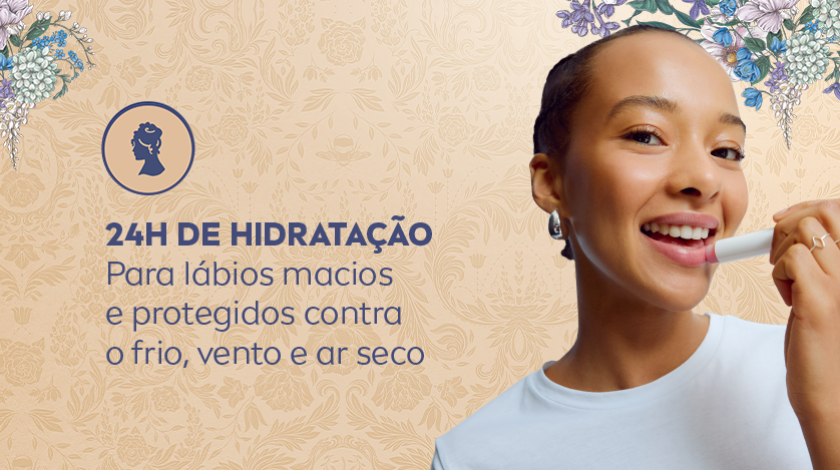 Mulher sorridente aplicando hidratante labial. O fundo é claro, com iluminação suave e elementos florais sutis em tons pastel, criando uma atmosfera delicada e acolhedora.
