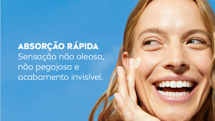 Mulher loira sorri, enquanto aplica o produto no rosto. O fundo é azul claro.