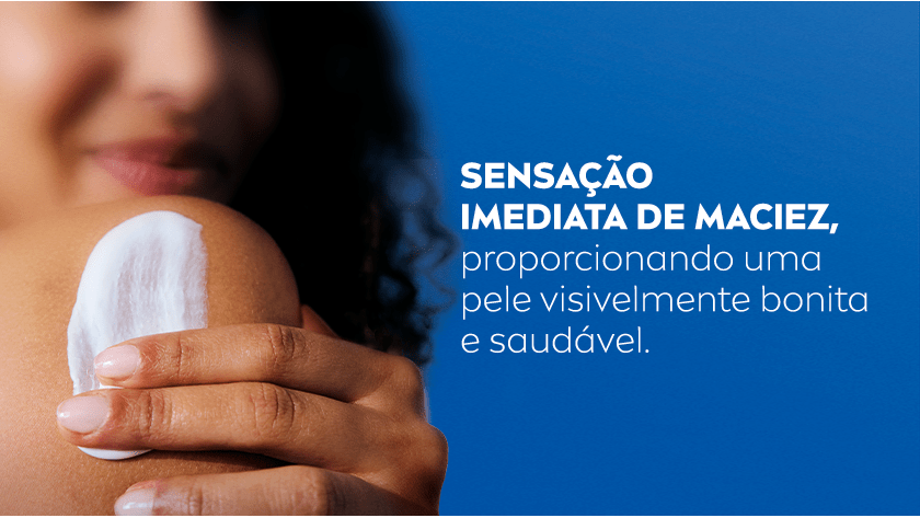 A imagem apresenta uma mulher em desfoque, aplicando o creme no ombro. O destaque fica na textura do produto em sua pele. O fundo é azul escuro.