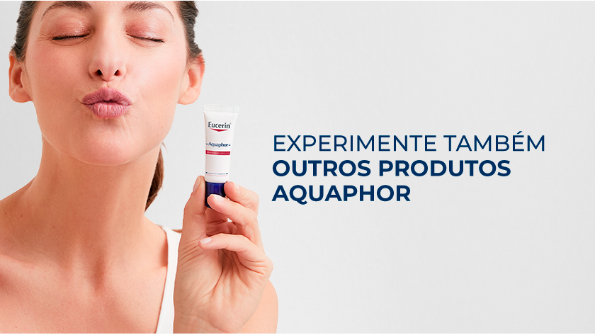 Fundo neutro. Ao lado esquerdo, uma modelo faz um beijo com os lábios, enquanto fecha os olhos. Ela segura o Aquaphor Labial ao lado do rosto.