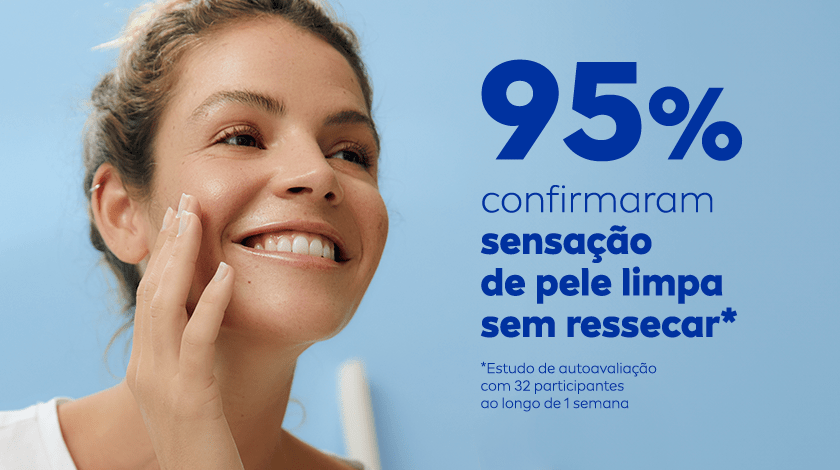 Mulher sorrindo e aplicando o produto no rosto. O fundo é azul claro.