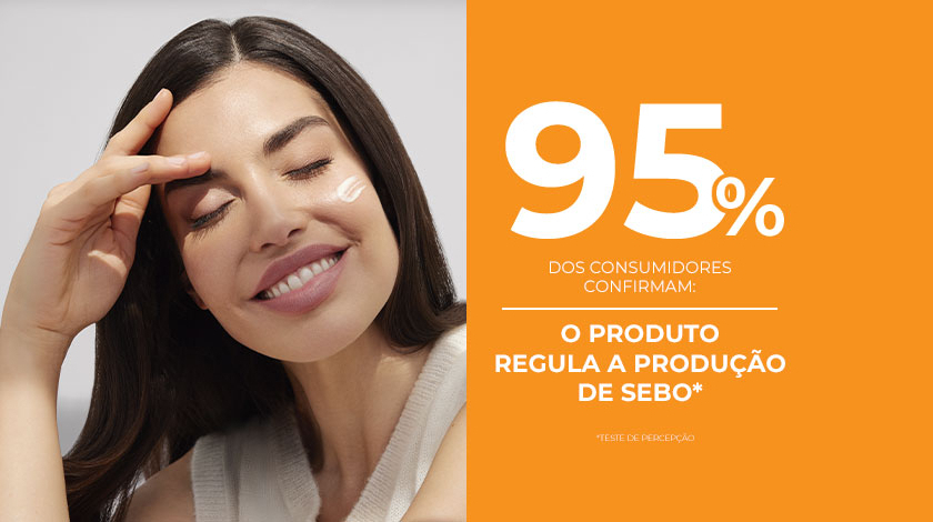 Uma mulher de pele saudável e radiante sorri enquanto toca o rosto, ao lado de um fundo laranja.
