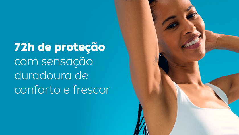 Uma mulher sorri, enquanto levanta os braços e exibe as axilas. Ela usa uma regata branca, e o fundo é um céu azul.