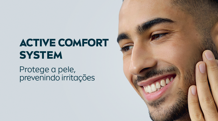 Imagem de um homem sorrindo, ao passar a mão no rosto. O fundo é cinza e neutro.