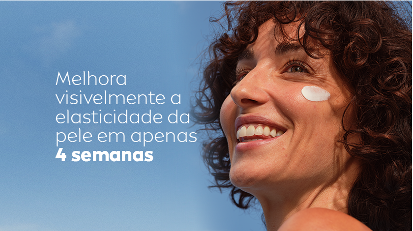 Mulher sorri enquanto olha para cima. Em seu rosto, está aplicado um pouco de creme. O fundo é um céu azul.