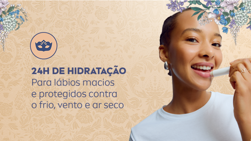 Mulher sorridente aplicando hidratante labial. O fundo é claro, com iluminação suave e elementos florais sutis em tons pastel, criando uma atmosfera delicada e acolhedora.