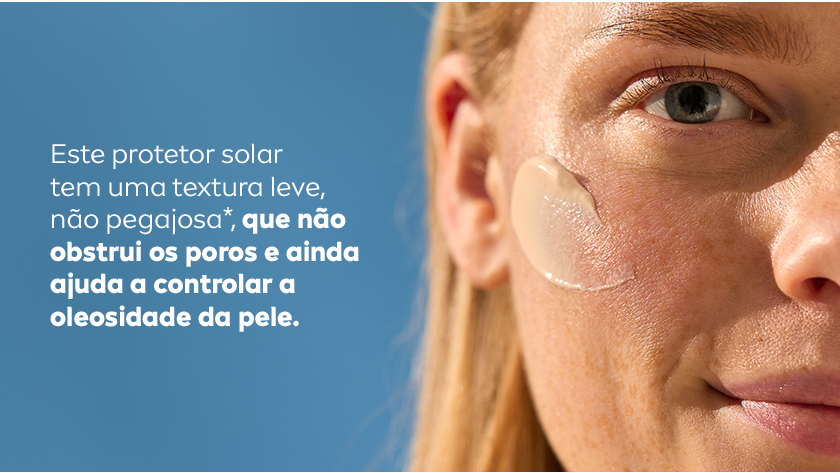 Imagem em close de uma mulher com o protetor solar aplicado no rosto. Fundo desfocado de cor azul.