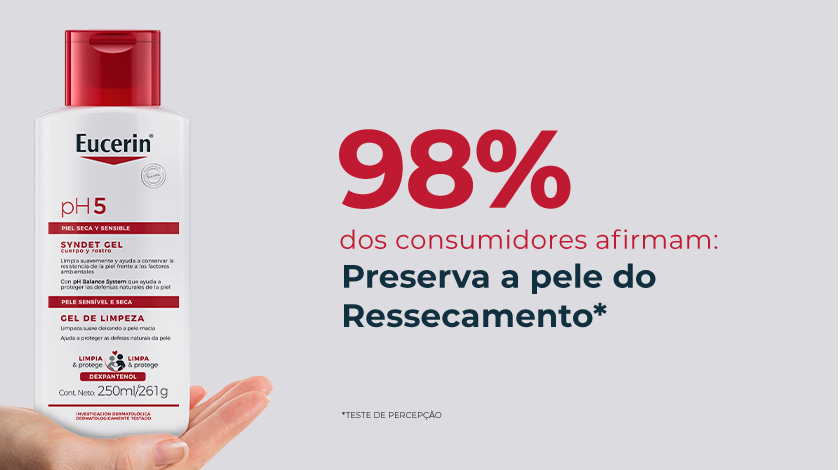 Imagem com fundo neutro. Ao canto esquerdo, uma mão segura delicadamente a embalagem do produto.