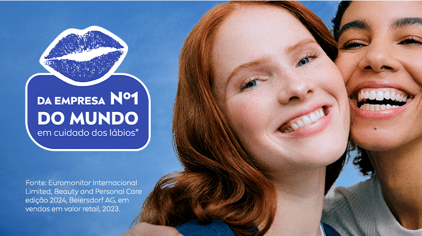 Imagem dividida em duas partes. À esquerda, um fundo azul com uma ilustração branca de um boca, como a marca de um beijo. À direita da imagem, duas mulheres aparecem sorrindo de forma espontânea. A da esquerda tem pele clara, olhos azuis, lábios rosados e usa um batom brilhante. A da direita tem pele escura, cabelos presos e um sorriso largo que mostra os dentes brancos. As duas estão bem próximas e com aparência de felicidade.