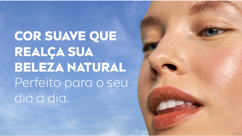 Mulher com expressão confiante e sorriso no canto dos lábios, olhando para o lado, fundo de céu azul.