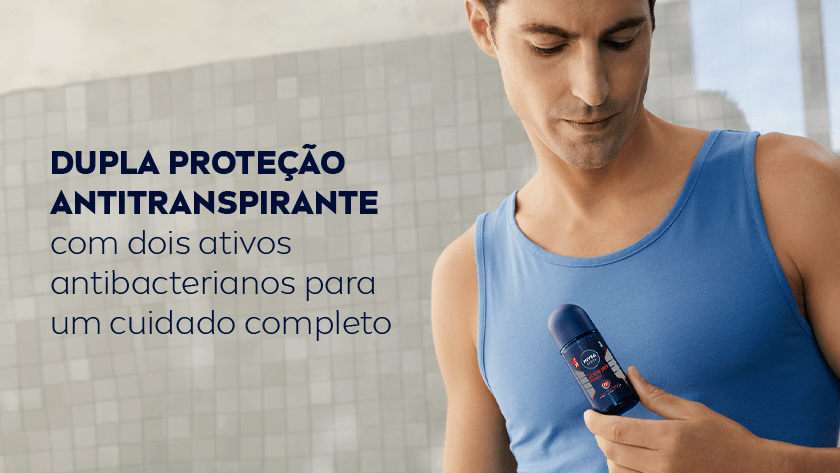 Homem usando regata azul segura desodorante roll-on NIVEA MEN Active Dry Impact no peito, em um ambiente com parede de azulejos cinza ao fundo. Ele olha para baixo, focado no produto.