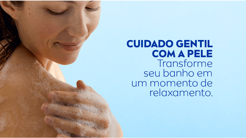 Mulher com expressão relaxada ensaboa o ombro com espuma abundante durante o banho, em um fundo azul claro.