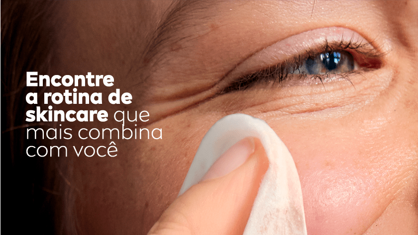 Close nos olhos de uma mulher sorrindo enquanto utiliza um lenço de limpeza no rosto.