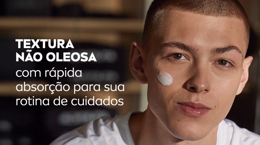 Homem jovem com pele clara aplicando NIVEA MEN Creme no rosto, sorrindo levemente. O fundo está desfocado.
