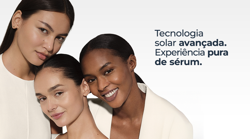 Três mulheres com diferentes tons de pele sorriem juntas, destacando peles iluminadas e saudáveis. Elas usam roupas brancas, com cabelos presos, em um fundo clean e minimalista.