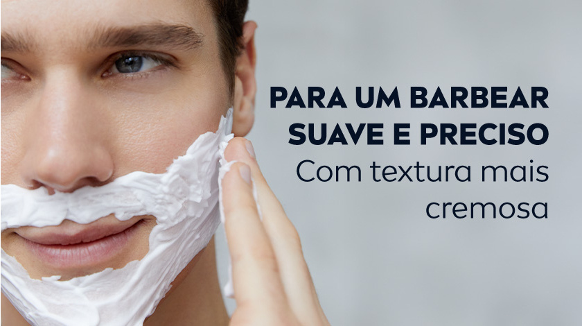 Homem aplicando espuma de barbear no rosto. O fundo é cinza claro.