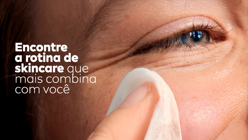 Close nos olhos de uma mulher sorrindo enquanto utiliza um lenço de limpeza no rosto.