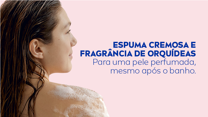 Mulher de pele clara e cabelos castanhos escuros molhados aparece sorrindo suavemente enquanto ensaboa o ombro com espuma. O fundo é rosa claro. À direita, há o texto da NIVEA em azul escuro.