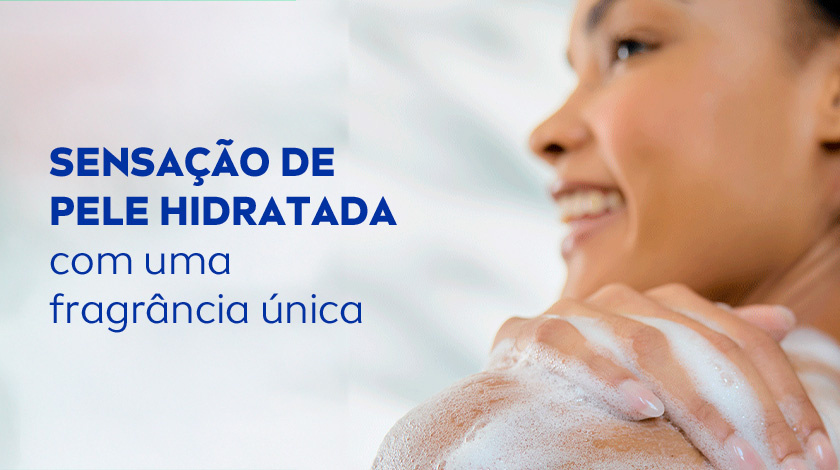 Sensação de pele hidratada com uma fragrância única Mulher negra sorridente de perfil, com ombros ensaboados, aplicando espuma no corpo durante o banho.