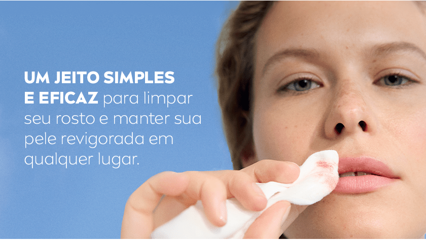 Mulher segura o lenço, enquanto passa nos lábios removendo a maquiagem. O fundo é um céu azul.