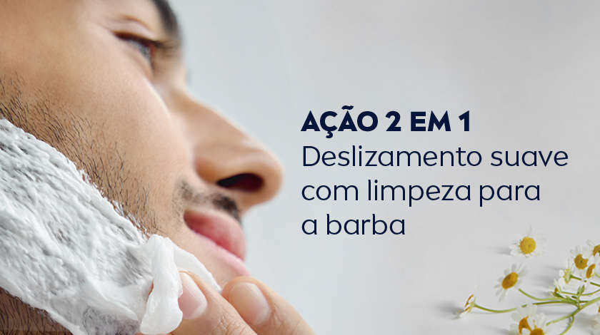 Homem passando creme de barbear no rosto. O fundo é cinza claro, e ao canto inferior direito aparecem flores de camomila.