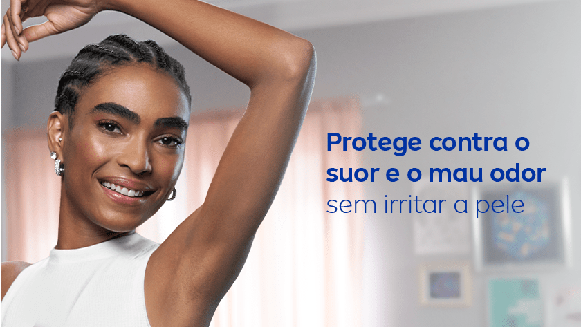 Protege contra o suor e o mau odor sem irritar a pele Uma mulher sorri, enquanto levanta o braço e exibe sua axila. Ela veste uma regata branca, e o ambiente é neutro.