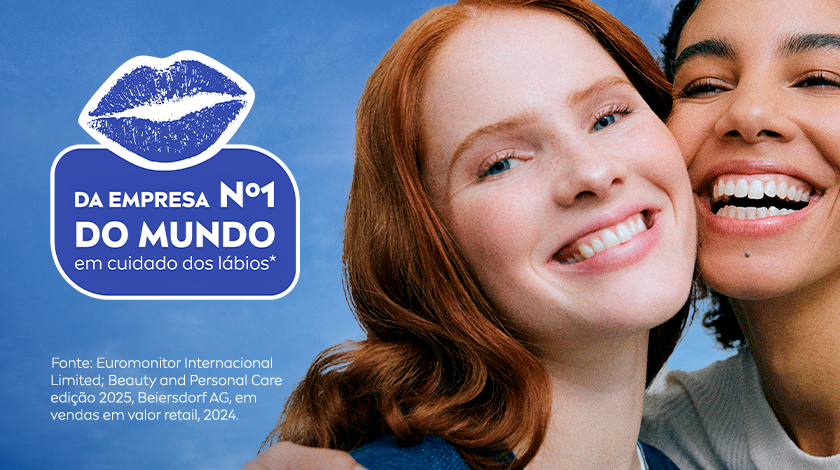 Imagem dividida em duas partes. À esquerda, um fundo azul com uma ilustração branca de um boca, como a marca de um beijo. À direita da imagem, duas mulheres aparecem sorrindo de forma espontânea. A da esquerda tem pele clara, olhos azuis, lábios rosados e usa um batom brilhante. A da direita tem pele escura, cabelos presos e um sorriso largo que mostra os dentes brancos. As duas estão bem próximas e com aparência de felicidade.