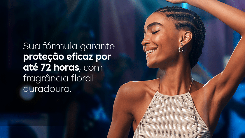 Imagem com fundo escuro e iluminação suave em tons azulados e roxos, remetendo a um ambiente de festa ou balada. À direita, uma mulher negra de cabelo trançado está sorrindo, com os olhos fechados e um dos braços levantados. Ela usa um top claro e brilhante.